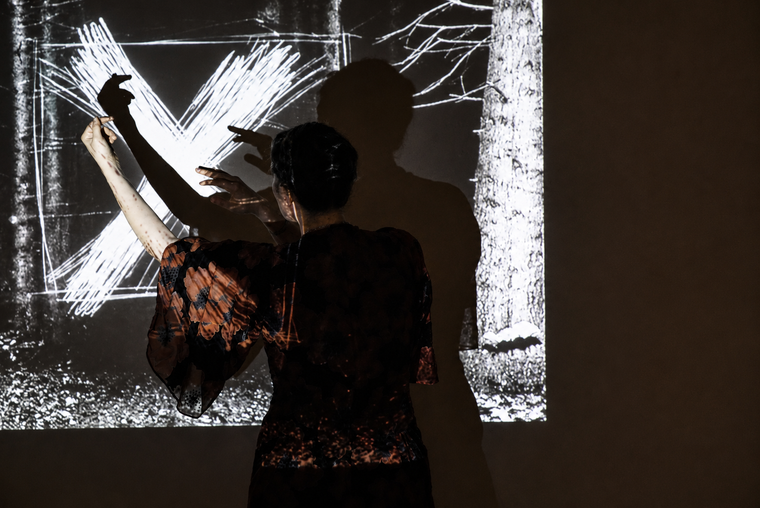 Performer reaching toward a projected forest and white X
